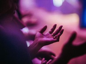 Crowd holding hands cupped upwards in church