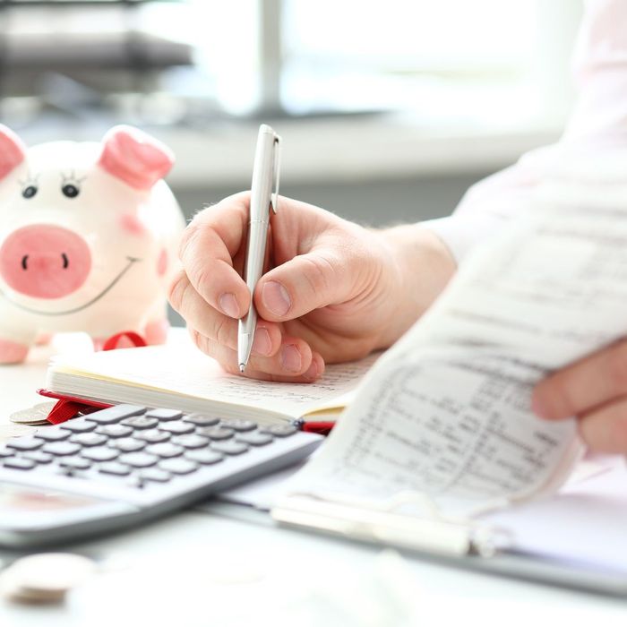 Person writing on financial documents with a calculator and piggy bank sitting beside them. 