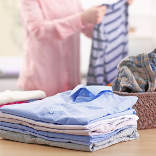 woman in pink shirt folding laundry into piles on a table
