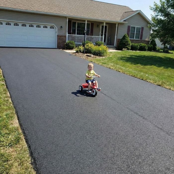 small child rides a tricycle on a smooth, newly repaired asphalt driveway