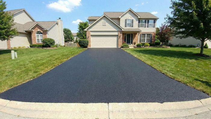 Wide angle view of a pristine, freshly sealed asphalt driveway leading to a nice suburban home