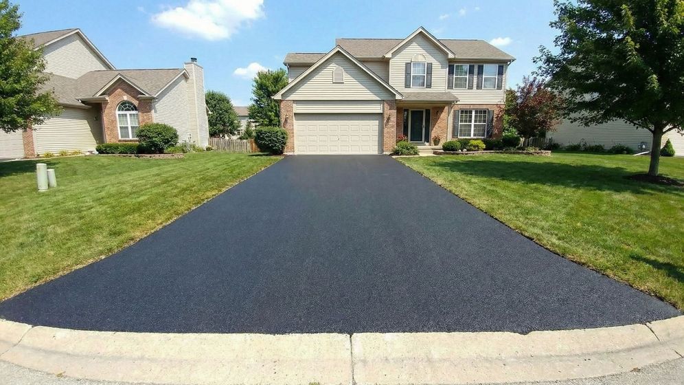 Wide angle view of a pristine, freshly sealed asphalt driveway leading to a nice suburban home