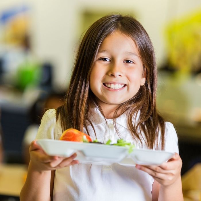 A girl holding school lunch and smiling.