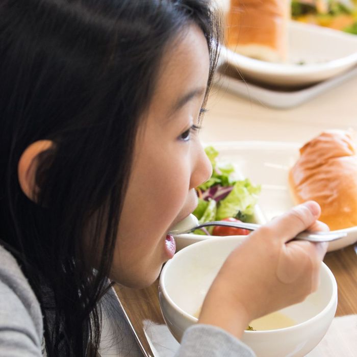 a child eating a school lunch of soup, salad and bread
