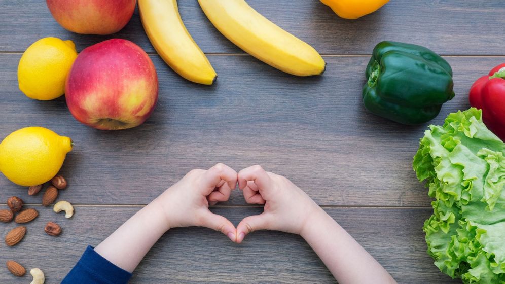 Fruit and veggies surround child's hands that are making a heart shape