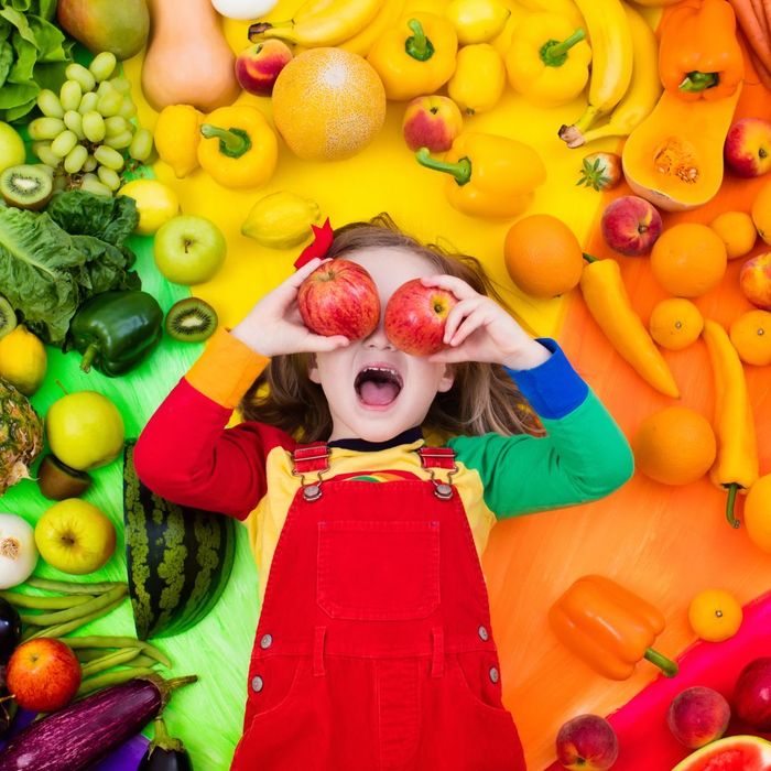 Young girl holds apples to her face, surrounded by color coded fruits and vegetables