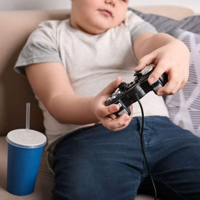an obese child sitting on the couch playing video games with a soda