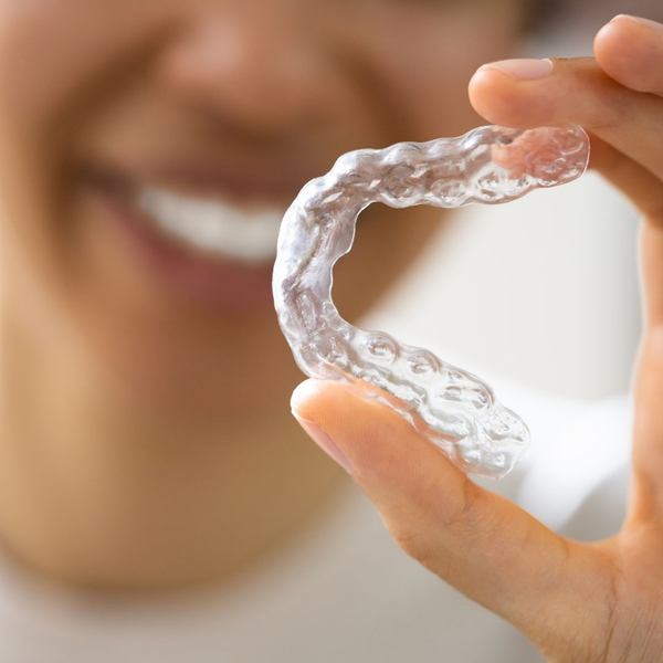 holding clear aligner up to camera, blurry smile in background