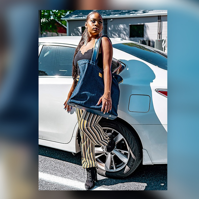 Black woman leaning against a car with the Shoelugg on her shoulder. 