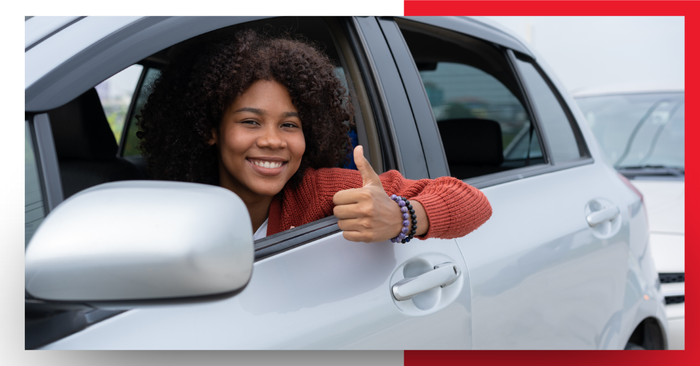 A woman in a car smiling with a thumbs up