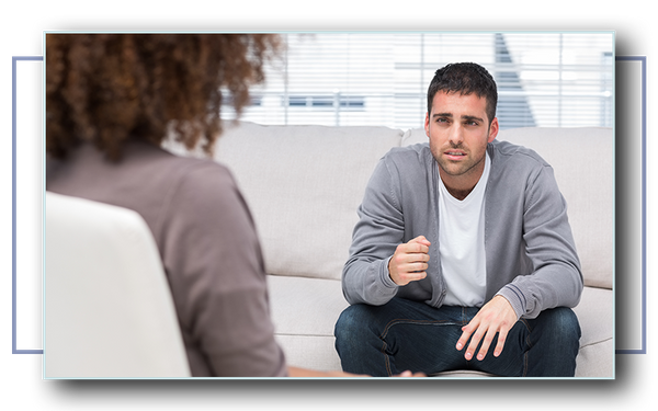 Sad-looking young man sitting on a couch speaking with a counselor.