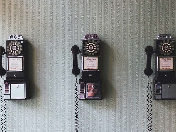 Three old rotary style telephones mounted on a wall next to each other