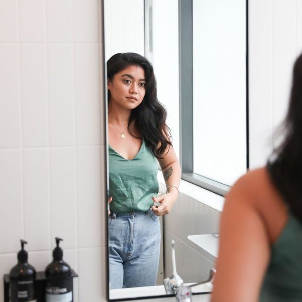 Woman in green top and jeans looking at herself in a bathroom mirror