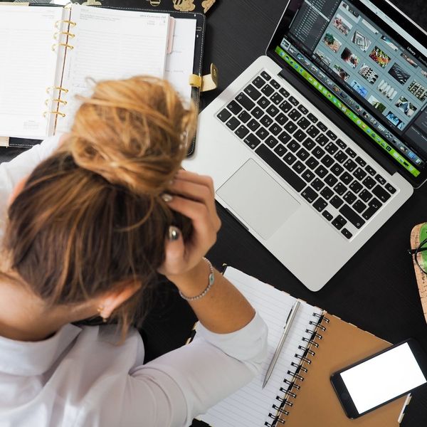 Woman holding her head while stressed about her workload in front of laptop