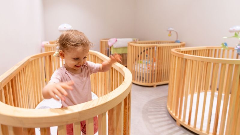 happy child standing in crib in a room with several cribs