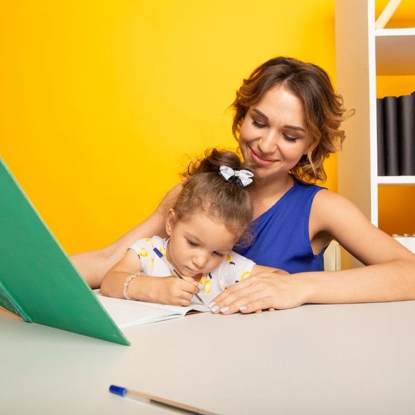daycare worker teaching young girl while she writes daycare worker teaching young girl while she writes