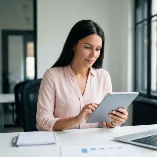 A focused professional sits in a sunlit office, reviewing automated sales performance data on a tablet device.