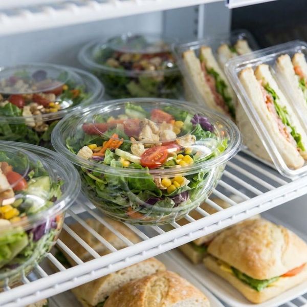 A close-up view shows a refrigerated display case stocked with fresh, vibrant salads and pre-made sandwiches ready for self-service selection.