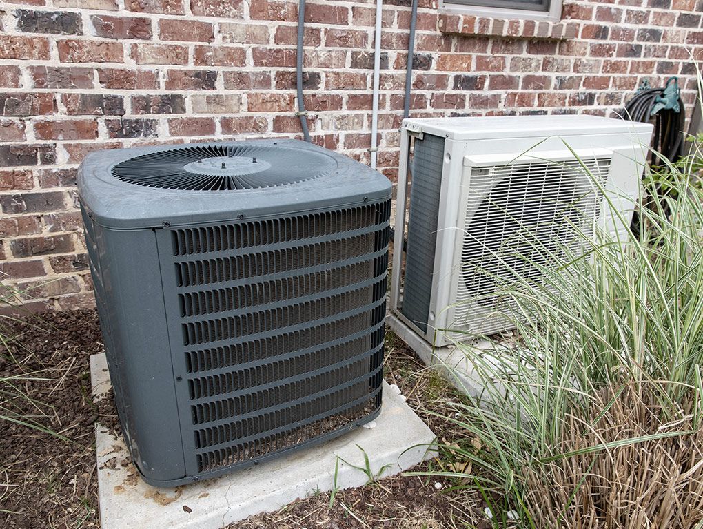 A residential air conditioning unit next to a brick wall