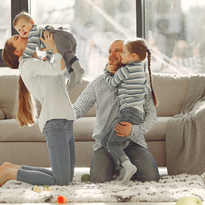 A happy family sits together on their living room floor