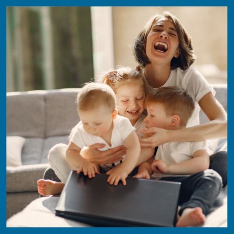 A happy mother on a couch holding her three children in her lap and laughing. 