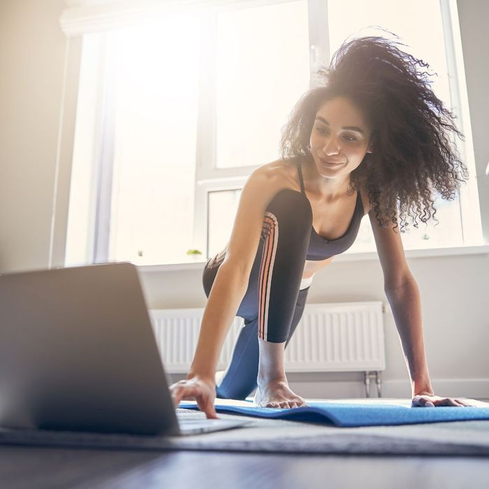 Woman working out on yoga mat in front of laptop