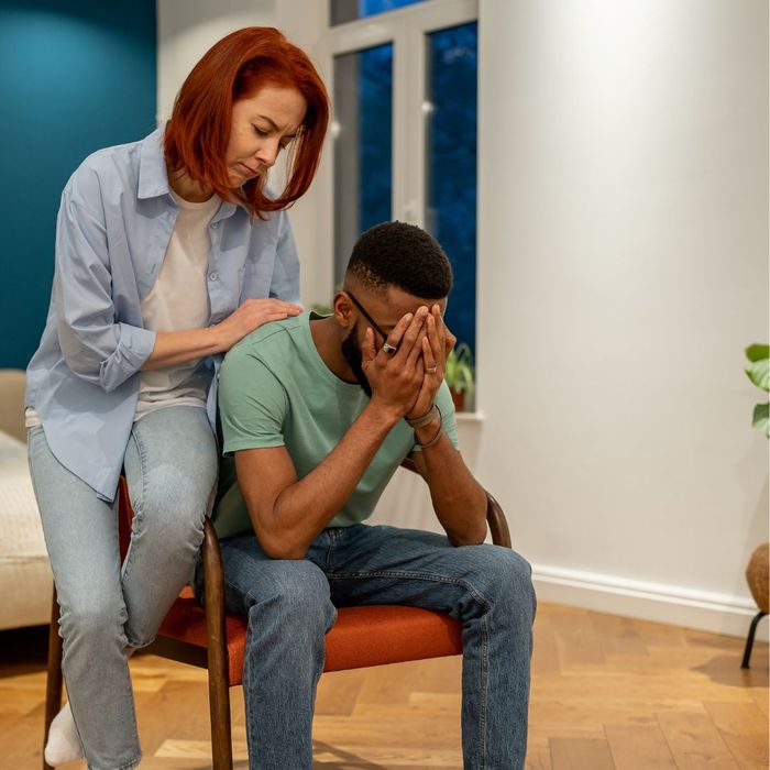 A woman comforting a man who is sitting with his head in his hands