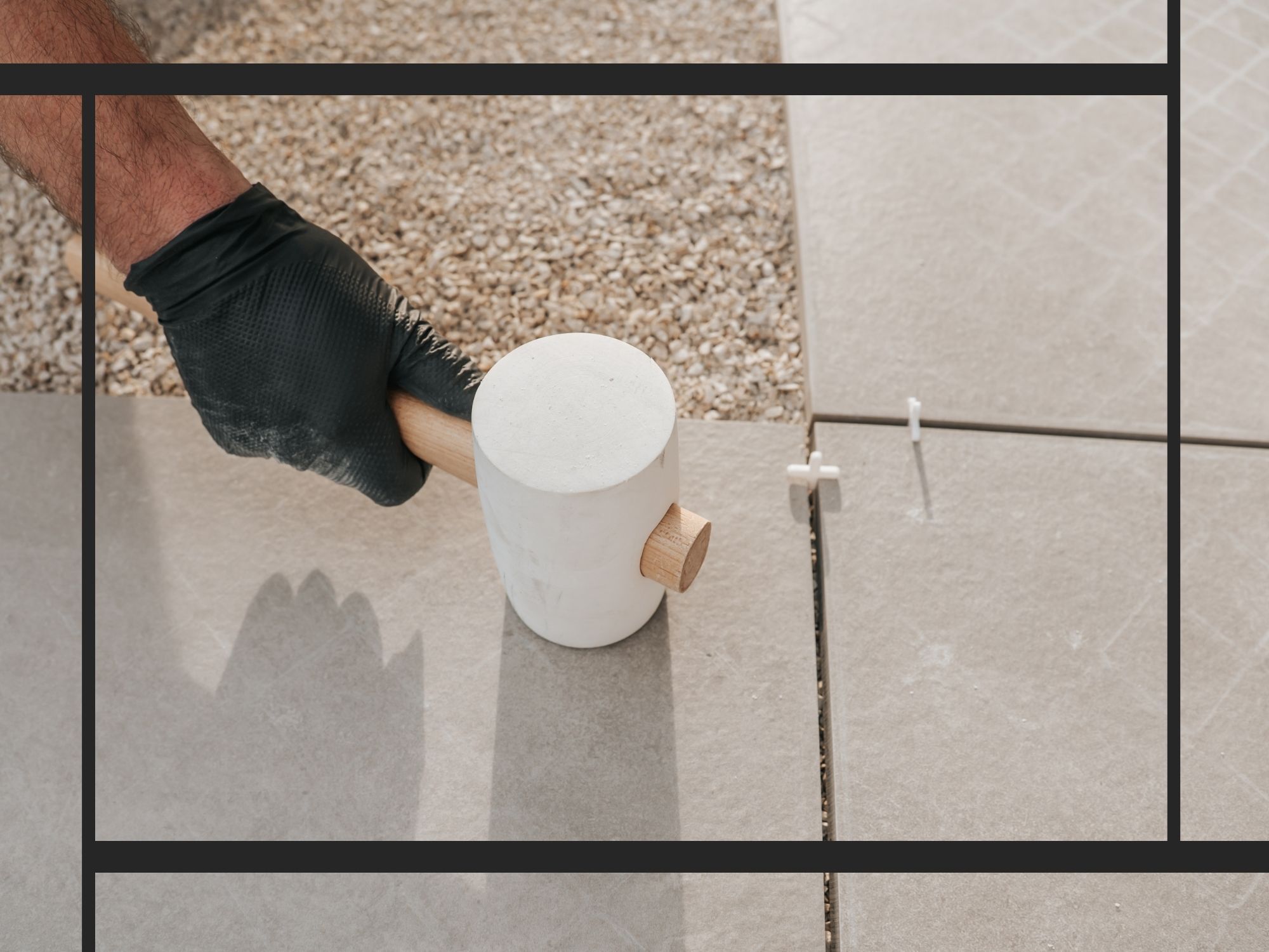 A detail-oriented shot of a contractor's hand in a black glove using a white rubber mallet to precisely level large-format gray floor tiles during installation.