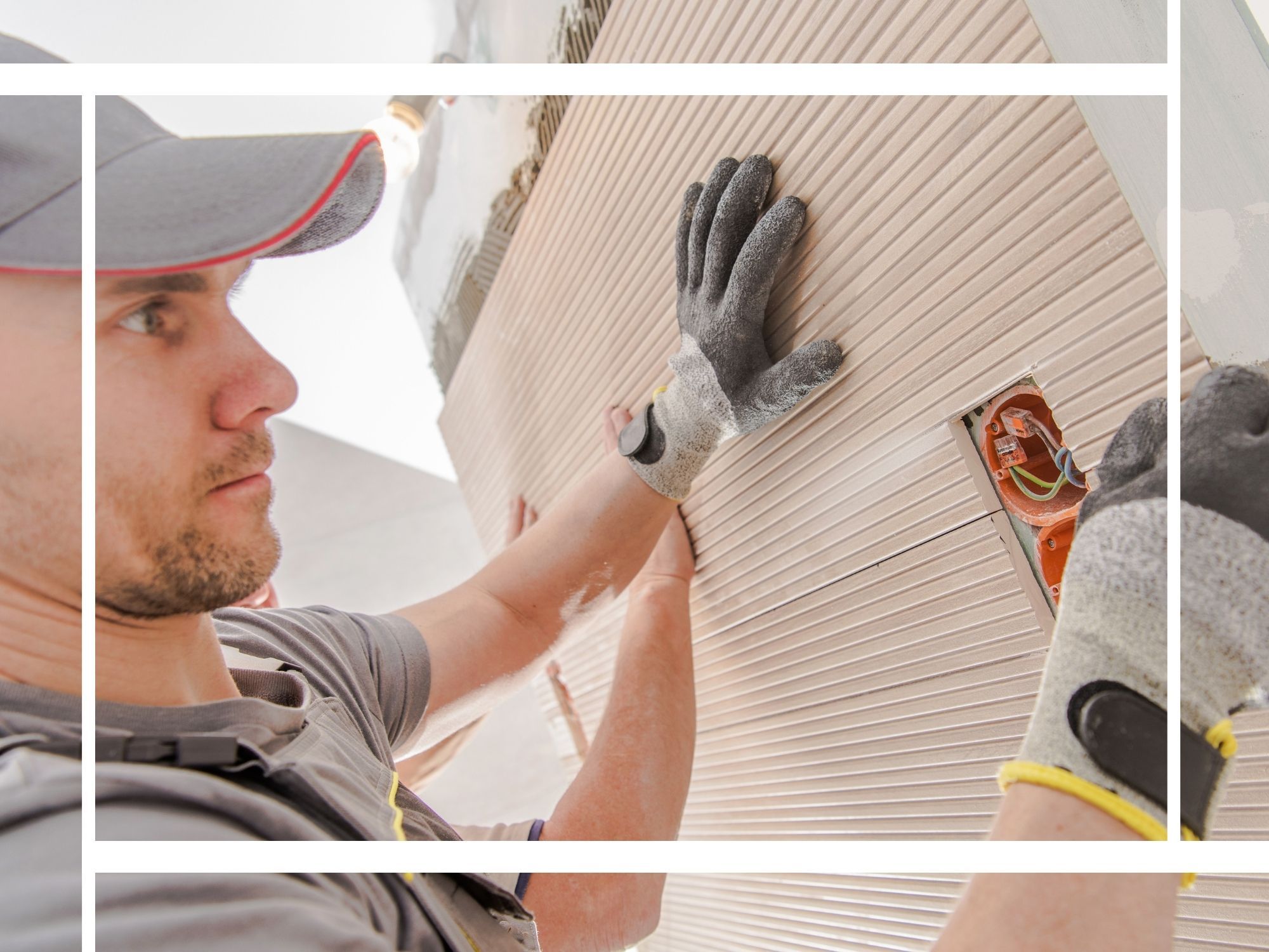 A professional tile installer in a gray uniform and cap carefully mounting a large, textured beige wall tile around an electrical outlet box