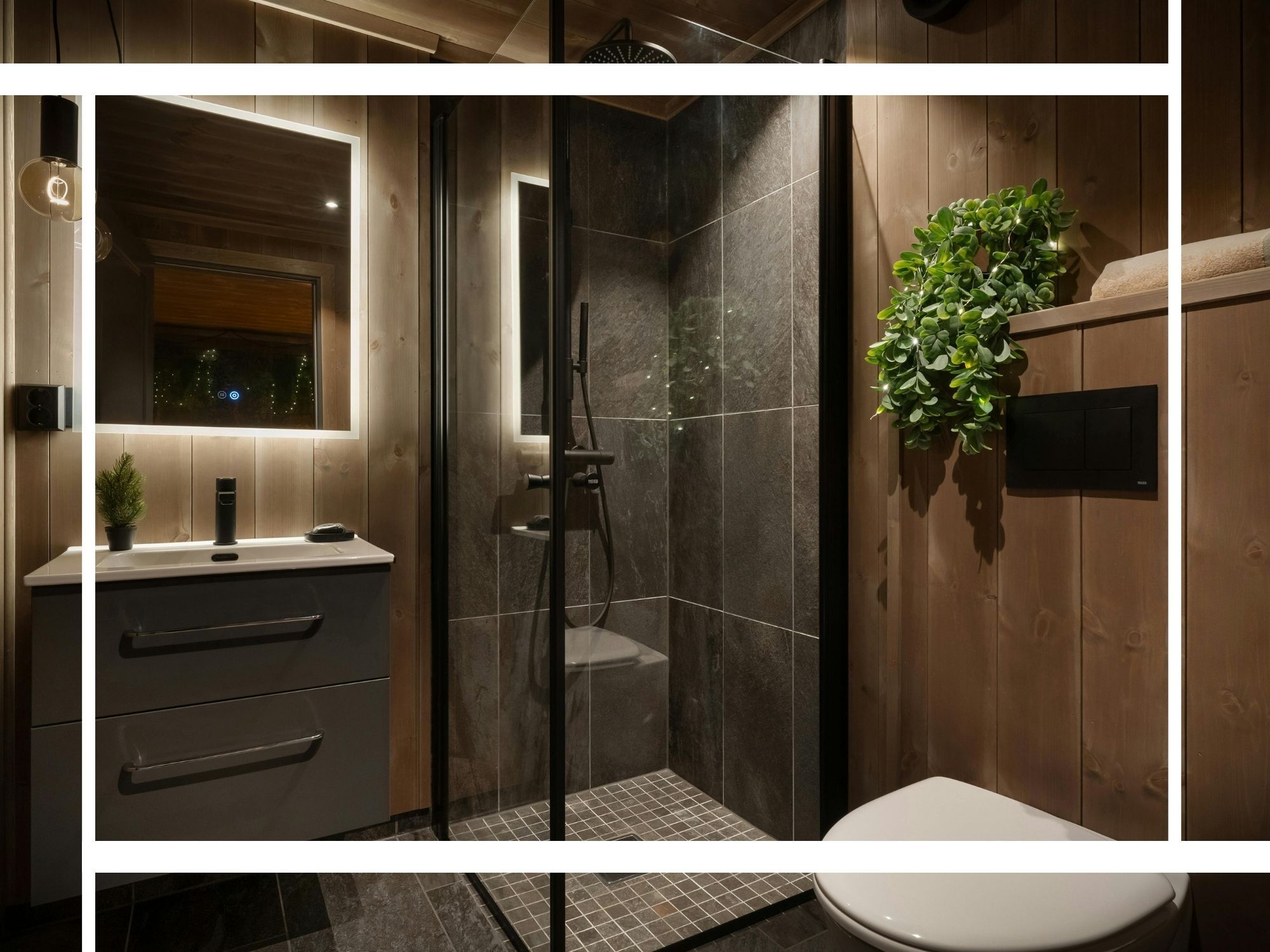A moody, spa-like bathroom featuring dark slate walk-in shower tiles, rustic wood-paneled walls, an illuminated LED mirror, and lush greenery for a relaxing atmosphere.