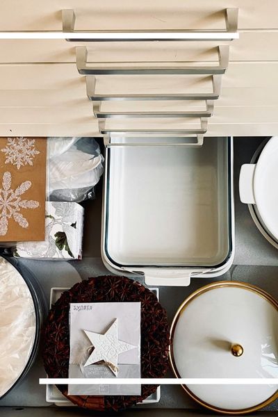 A top-down organizational shot of a clean kitchen drawer containing white ceramic baking dishes, festive decor, and sleek modern brushed-metal handles