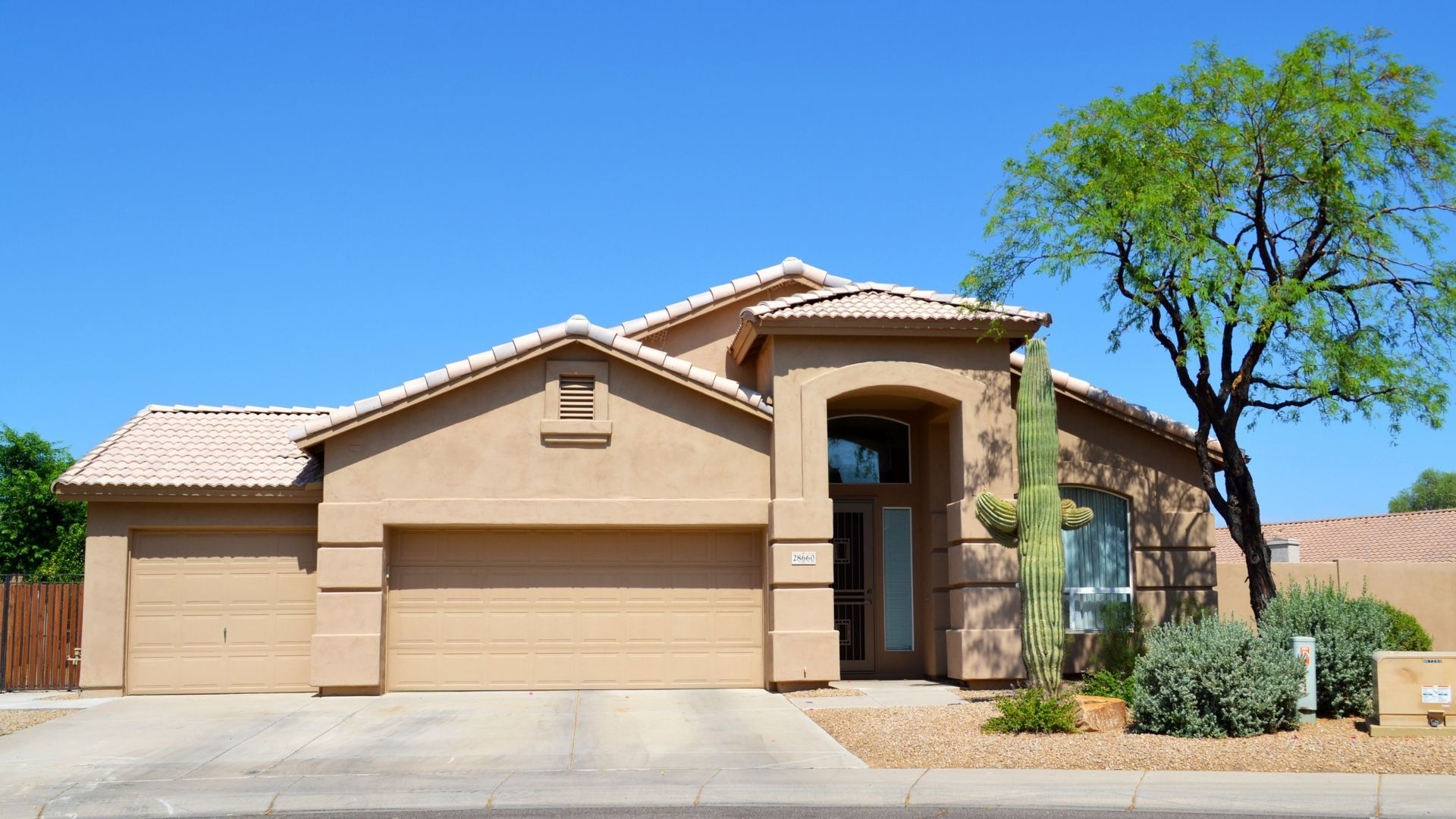 A professional exterior shot of a tan stucco Arizona home with a red tile roof, featuring a large Saguaro cactus and desert landscaping