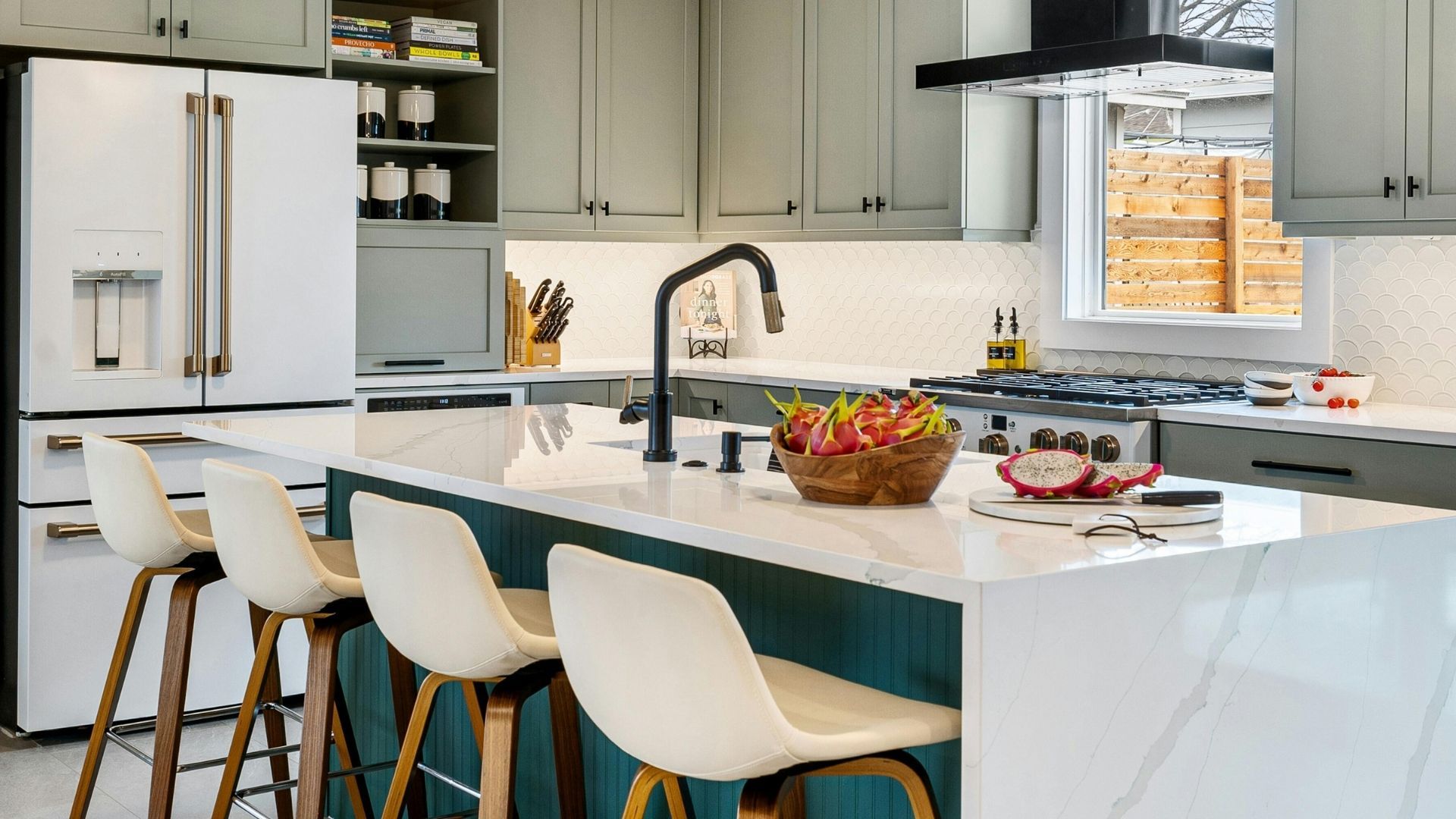 A luxury gourmet kitchen with a large marble-waterfall island, teal accent paneling, sage green cabinetry, high-end white appliances