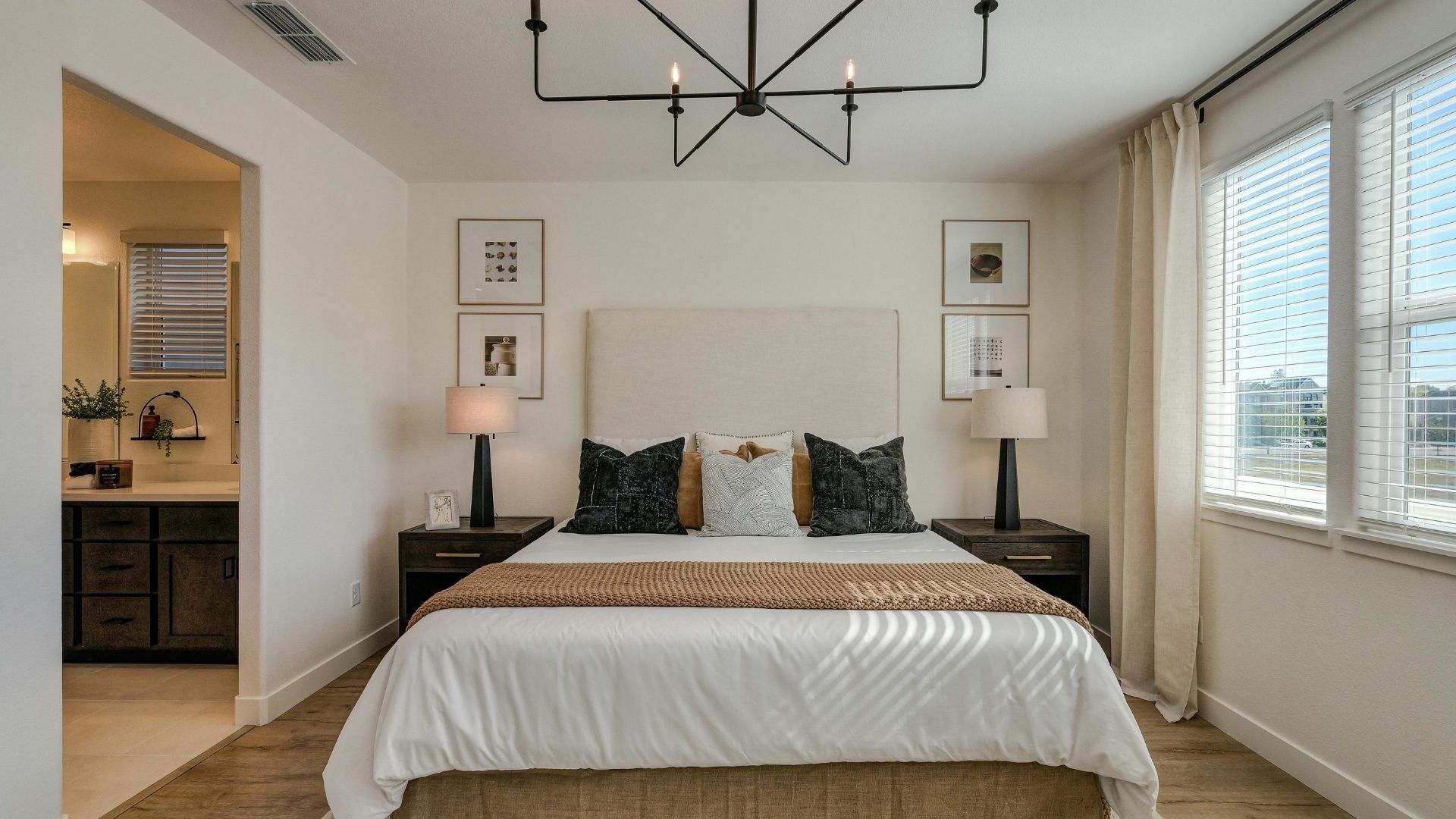 A bright, high-end master bedroom addition featuring a neutral upholstered headboard, modern black bedside lamps, and large windows that fill the space with soft, natural light