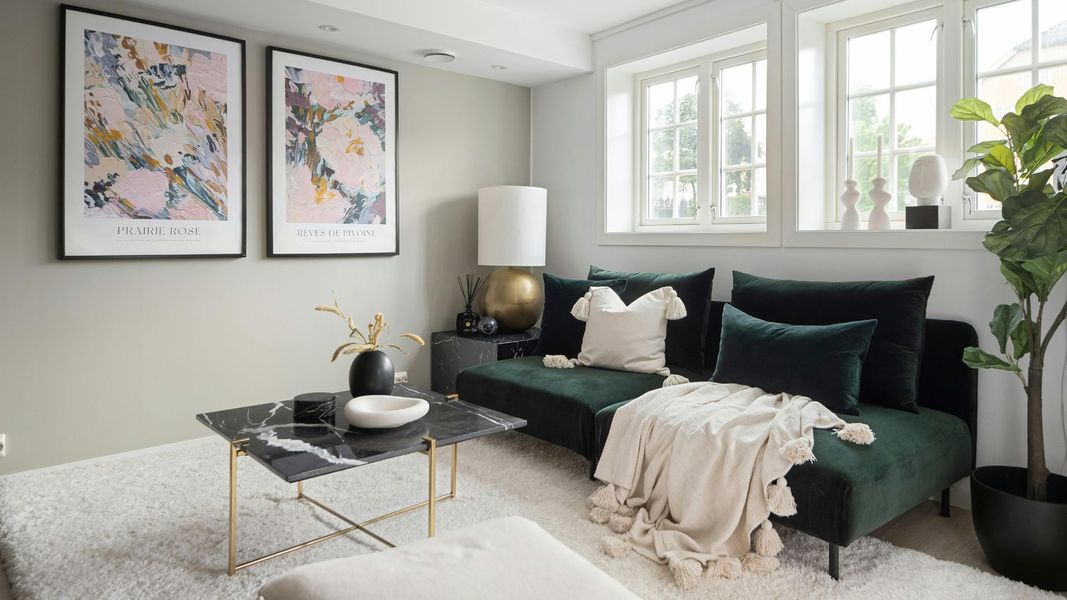 A modern, luxury living room featuring a deep forest green velvet sectional sofa, a black marble coffee table, and large-scale floral abstract wall art under soft natural window light.