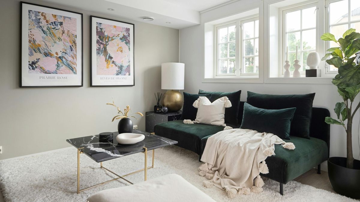 A modern, luxury living room featuring a deep forest green velvet sectional sofa, a black marble coffee table, and large-scale floral abstract wall art under soft natural window light.