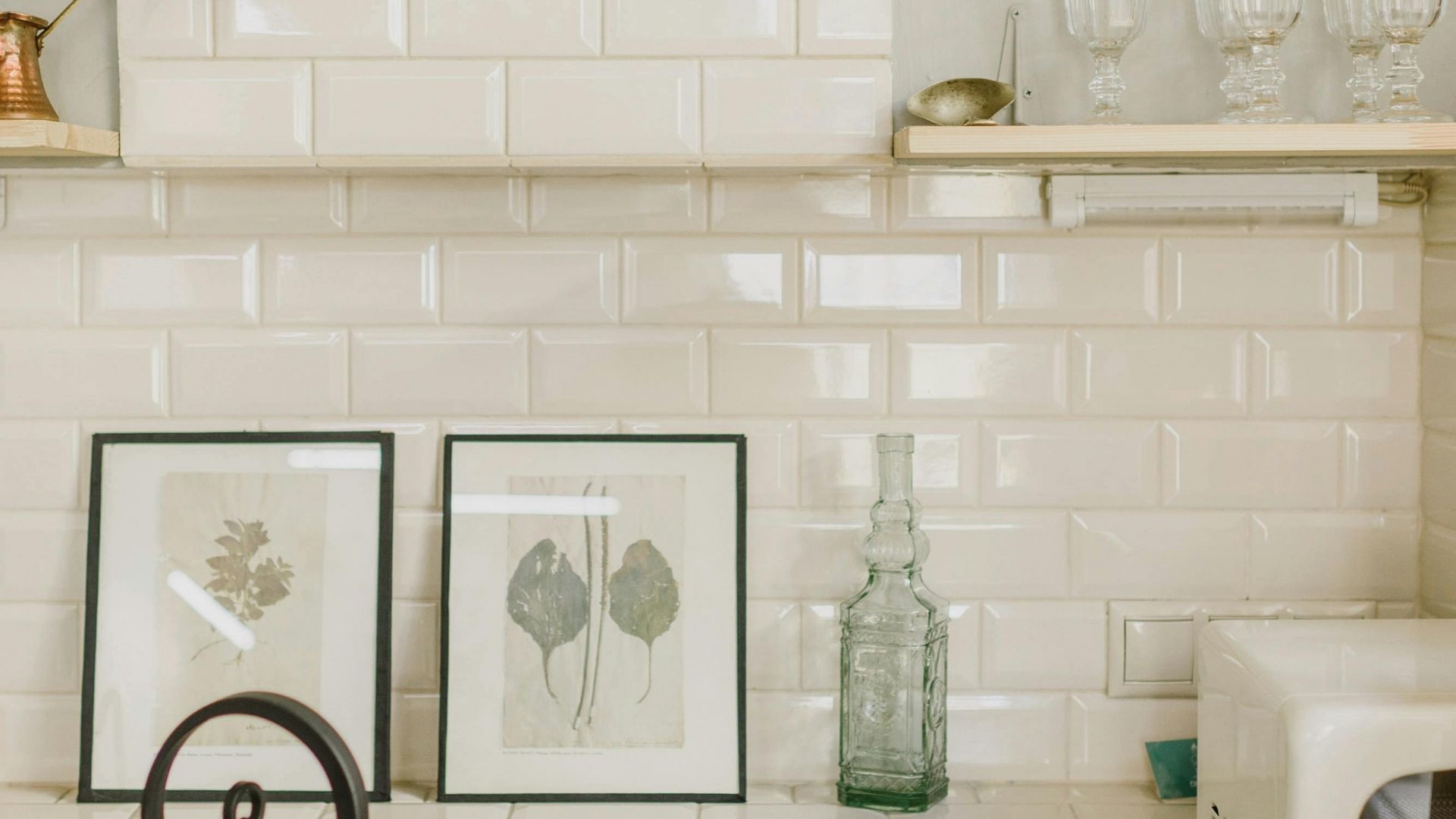 elegant kitchen backsplash featuring glossy white beveled subway tiles, decorated with framed botanical art and a vintage glass bottle