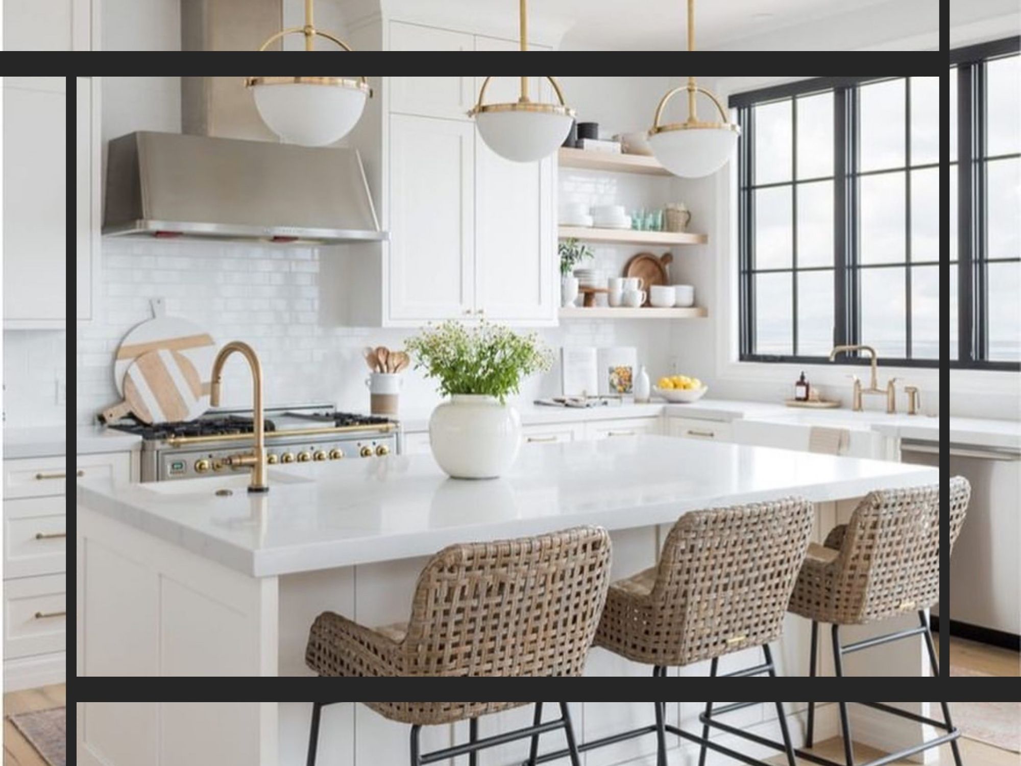 A bright, upscale white kitchen featuring a large marble island with woven barstools, gold globe pendant lighting, and a black-framed window
