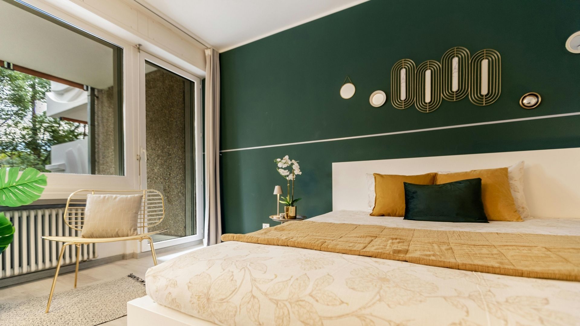 modern bedroom featuring a deep emerald green accent wall with gold geometric decor, a white upholstered bed