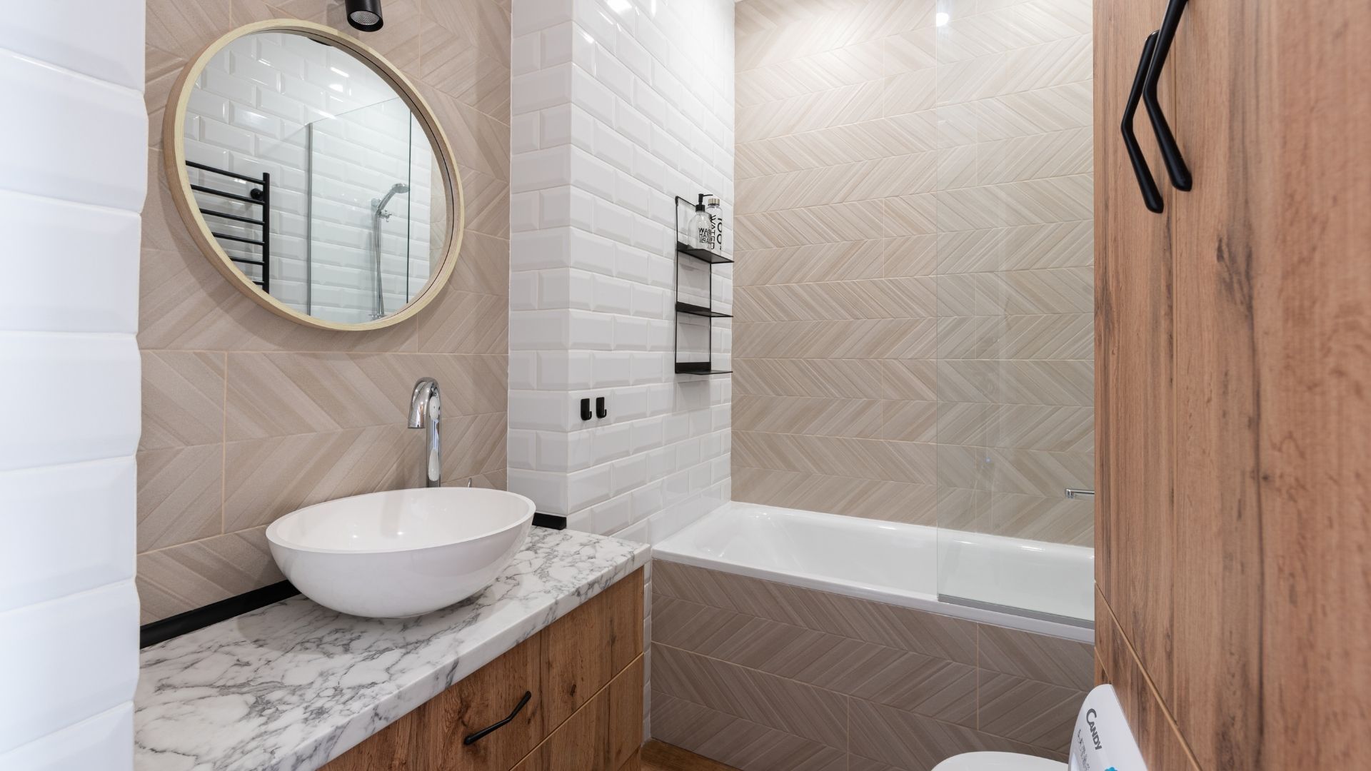 A contemporary bathroom design showcasing a vessel sink on a marble-topped oak vanity, complemented by a round mirror and a combination of white subway and beige chevron-patterned wall tiles