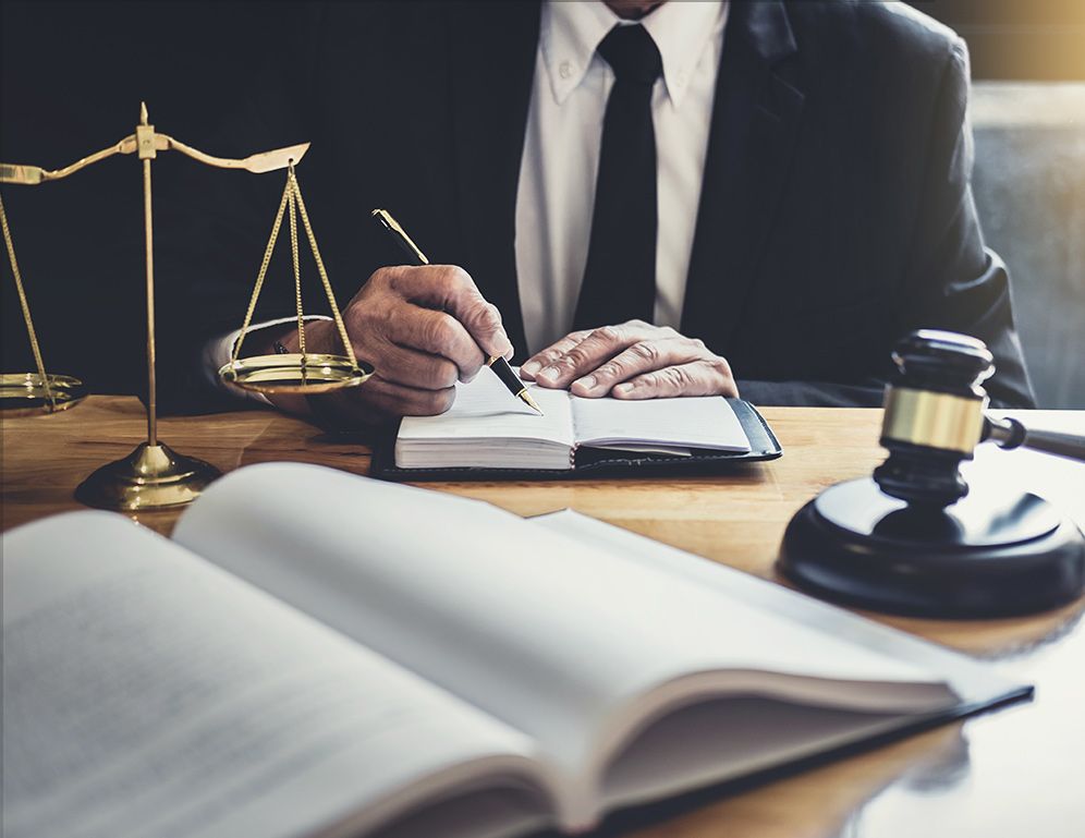 a person talking notes in front of a book with a gavel and a scale of justice on the table