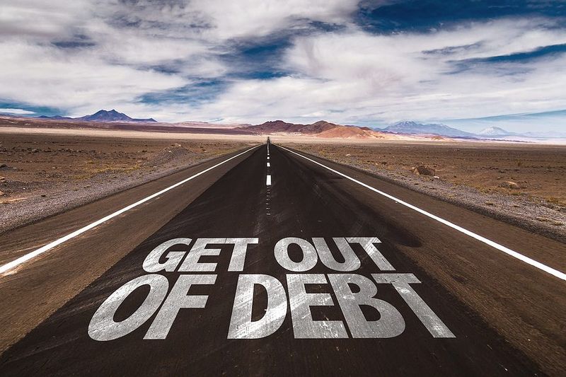 Open desert highway with "Get Out of Debt" painted on the road, representing debt reduction and financial freedom — J. Martin Wealth Management, Arizona. Desert highway with "Get Out of Debt" road markings