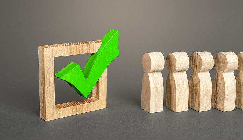 Wooden figures in line next to a green checkmark in a square frame.