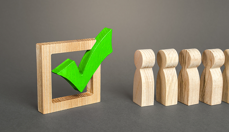 Wooden figures in line next to a green checkmark in a square frame.