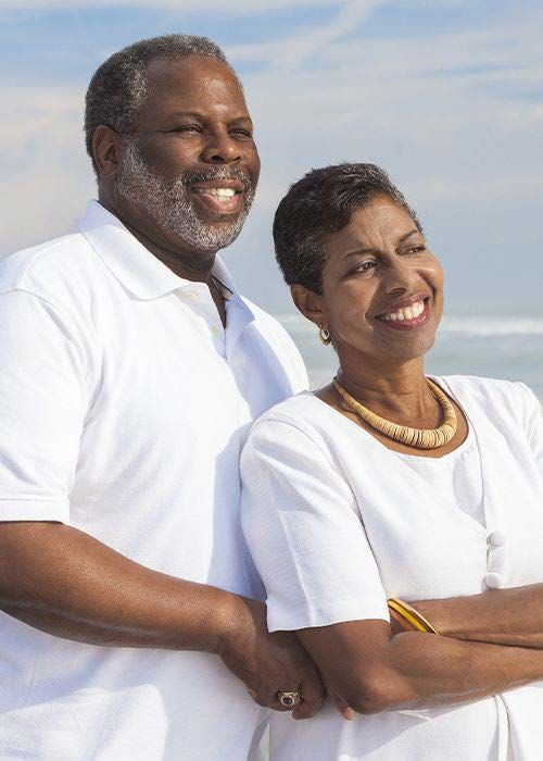 Smiling retired couple standing together on the beach, symbolizing confidence in retirement and financial independence