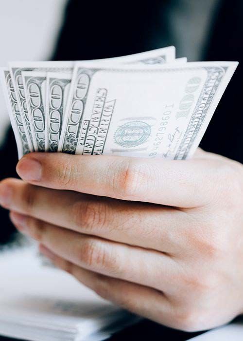 Hand holding several $100 bills, representing income planning, budgeting, and cash flow management for financial goals