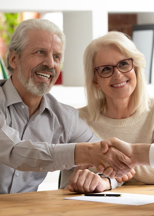 A happy retirement age couple shaking hands with a person over paperwork