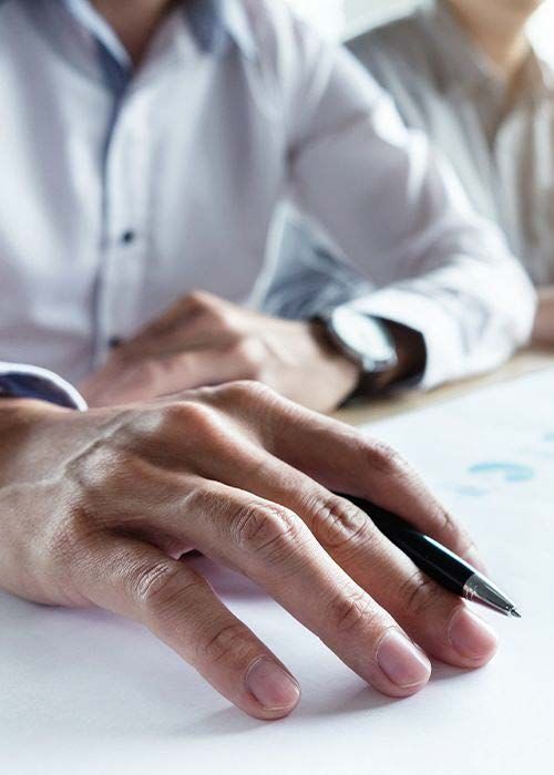 Close-up of hand holding pen during financial meeting, representing tax planning, strategy, and advisory services