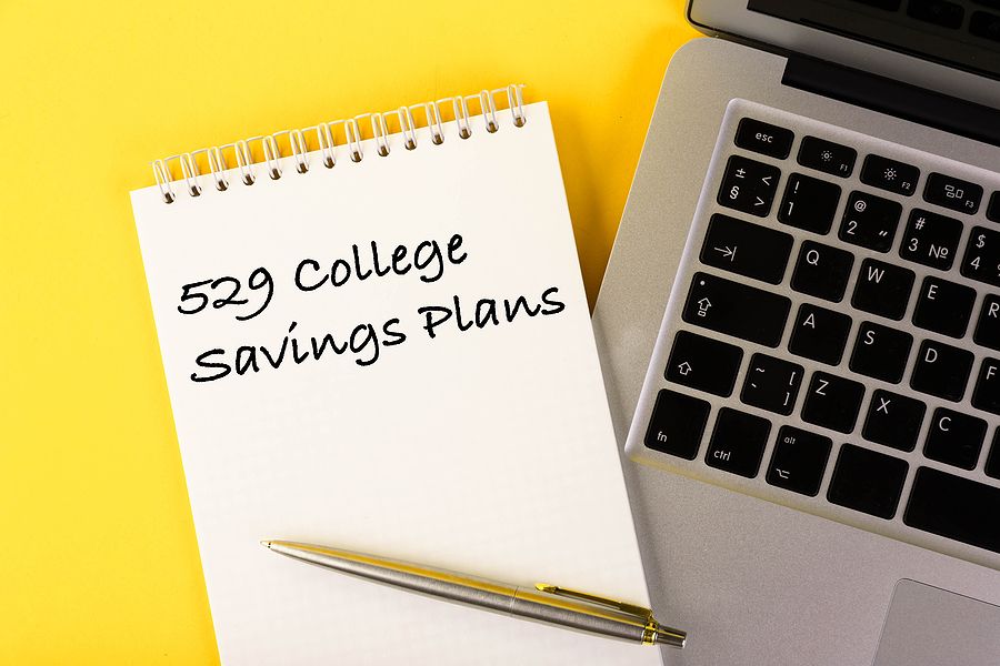 Notebook with 529 College Savings Plans written on it, next to a laptop and pen on a yellow background