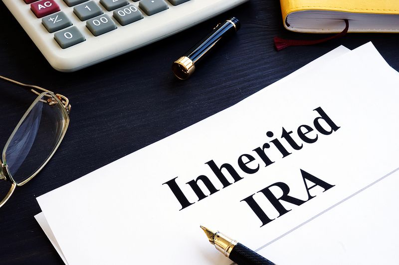 Inherited IRA paperwork on desk with calculator, glasses, and fountain pen, representing estate and retirement account planning